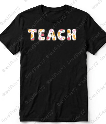 A black short-sleeve crewneck t-shirt featuring the word 'TEACH' printed across the chest in a playful, colorful patterned font with pink, orange, yellow, and white details. The t-shirt is displayed flat against a white background with diagonal 'Grand Print YJ' watermarks.