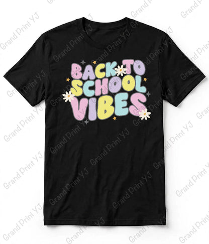 A black short-sleeve t-shirt with a colorful retro-style 'BACK TO SCHOOL VIBES' graphic on the chest, featuring pastel letters and small white daisy flowers, displayed flat against a white background with diagonal watermarks.