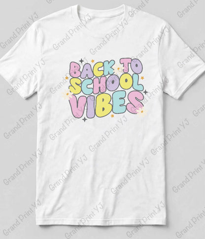 A white short-sleeve crewneck t-shirt featuring a colorful retro-style graphic that reads 'BACK TO SCHOOL VIBES' in pastel bubble letters with small star accents, displayed flat against a light gray background with diagonal watermarks.