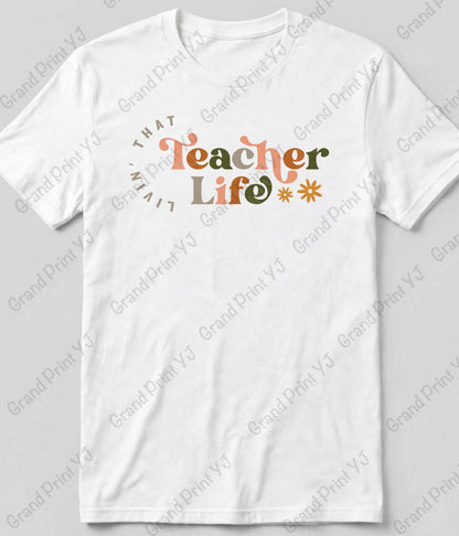 A white short-sleeve t-shirt with a graphic on the chest that reads 'THAT Teacher Life' in orange and olive green lettering, surrounded by a circular 'TEACHER' text and small starburst accents. The t-shirt is displayed flat against a light gray background with diagonal watermarks.