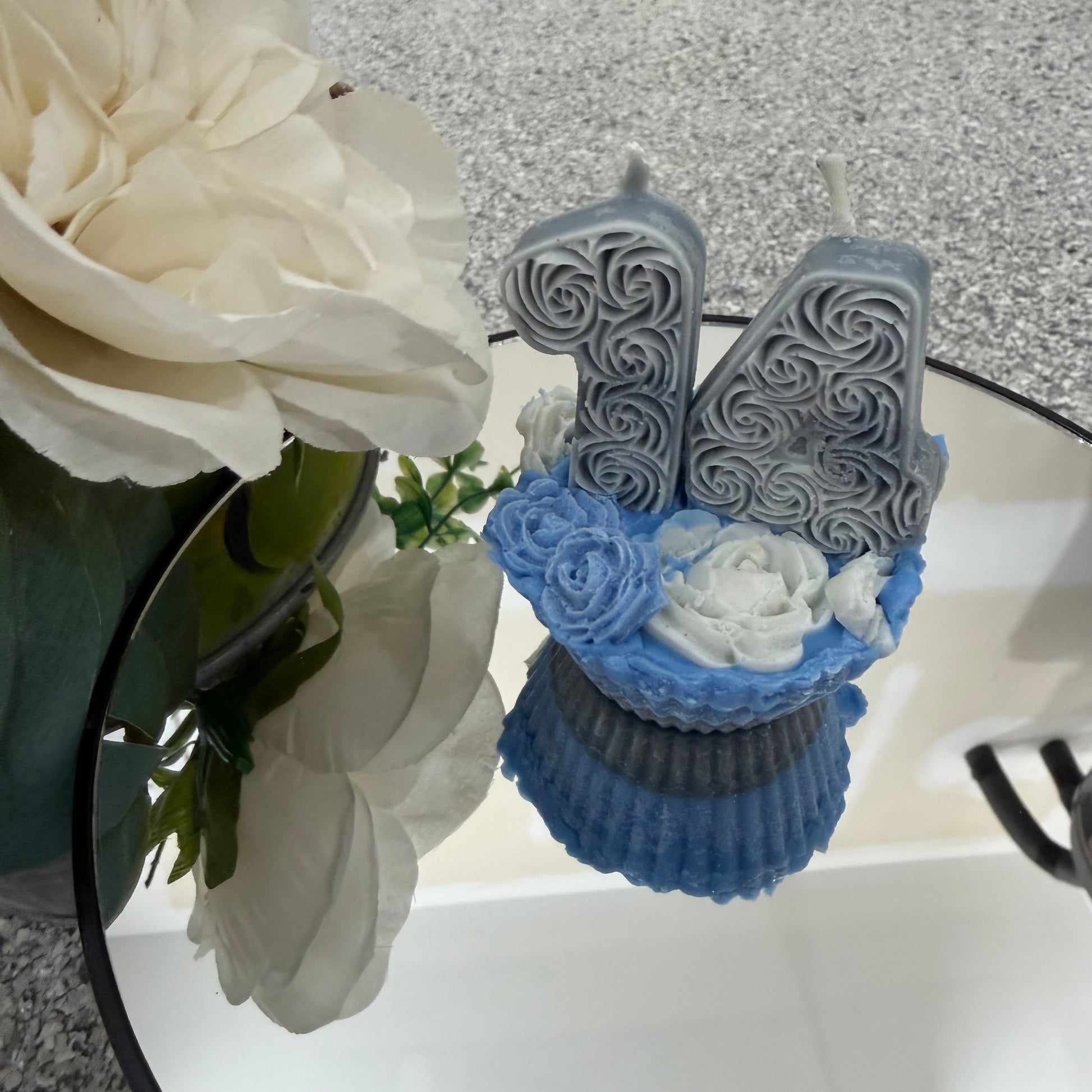 Decorative number '14' candle with blue cupcake and white flowers on a textured surface.
