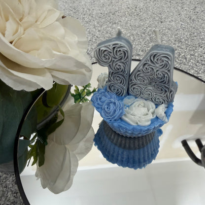 Decorative number '14' candle with blue cupcake and white flowers on a textured surface.