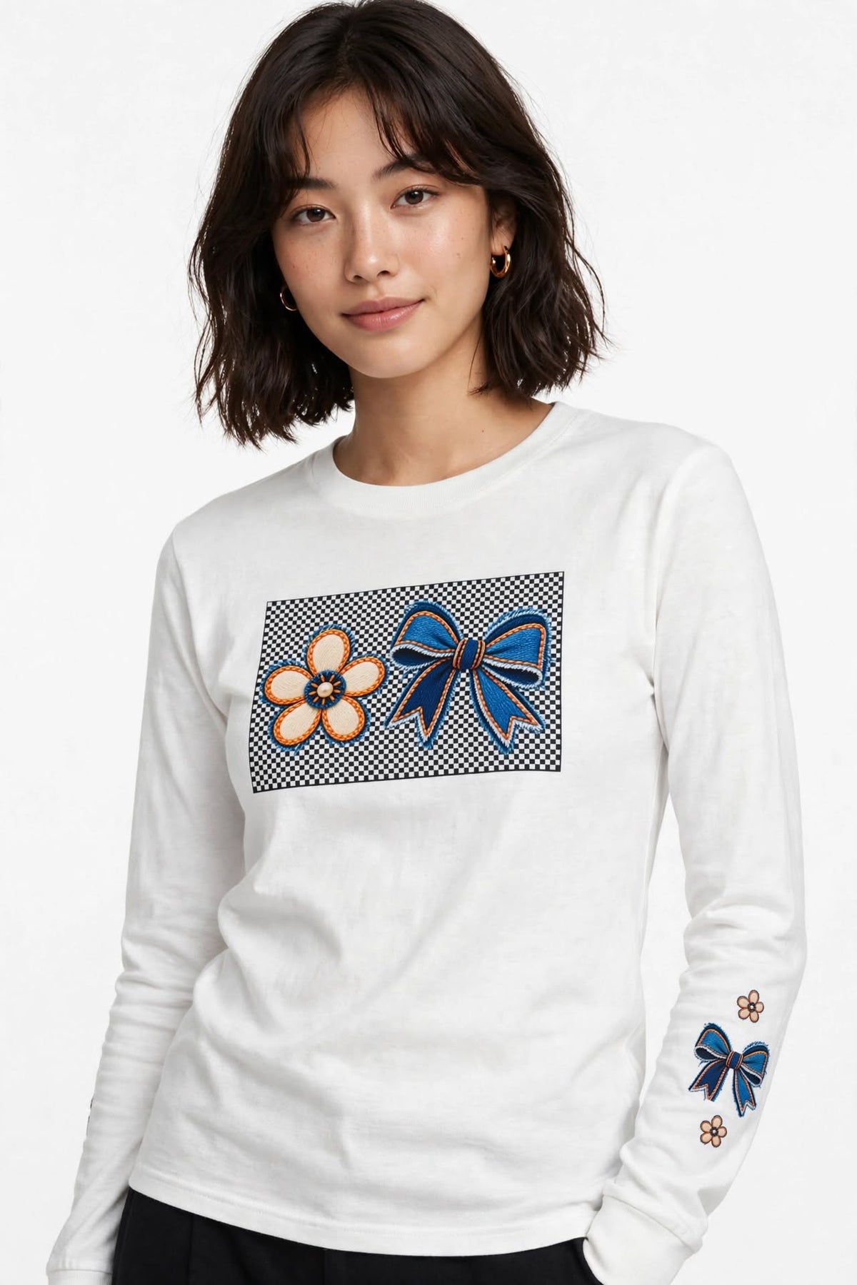 Graphic shirts near me - clothes shop near me. A woman wearing a white long-sleeve crewneck shirt with a graphic print on the chest featuring a blue bow and a flower, and matching blue bow graphics on the sleeve.