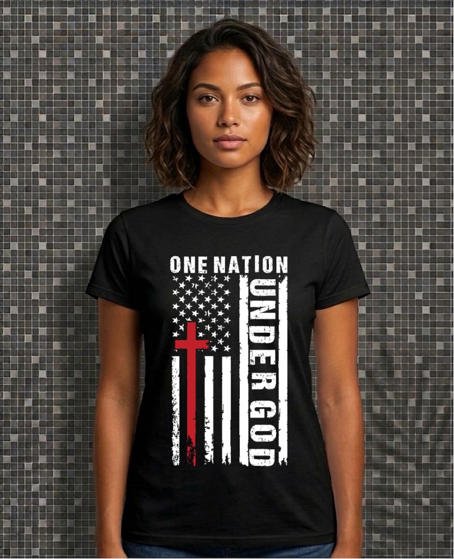 Person wearing a black t-shirt with an American flag and cross design, text 'One Nation Under God' on a patterned wall background.